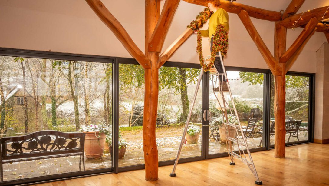 lady on a ladder hanging tinsel on a wooden beam